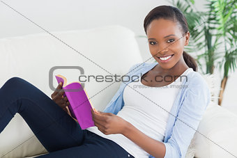 Black woman sitting on a sofa while holding a book