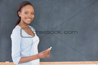 Black woman holding a chalk next to a blackboard