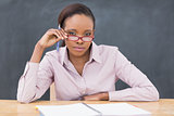 Serious teacher sitting at desk while touching her glasses
