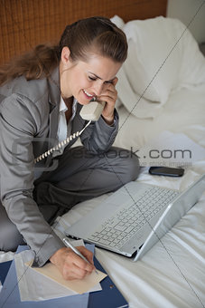 Smiling business woman having working phone calls on bed in hote