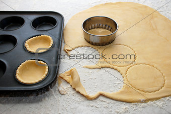 Pastry circles being cut and filling a bun tin to make jam tarts