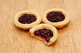 Three jam tarts, one with a bite taken, on a wooden table