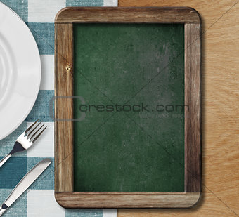 Menu blackboard lying on table with plate, knife and fork