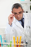 scientist touching his glasses behind test tubes in a laboratory