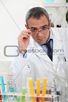 scientist touching his glasses behind test tubes in a laboratory