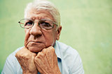 Portrait of serious old man looking at camera with hands on chin