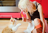 Beautiful blonde girl with candy in hand and cat sitting on kitchen floor
