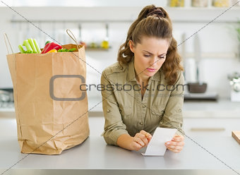 Concerned housewife checking bill after shopping in kitchen