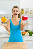 Happy young woman juggling with bell peppers in kitchen