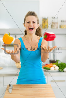 Happy young woman juggling with bell peppers in kitchen