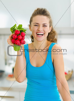 Smiling young woman holding bunch of radishes in kitchen