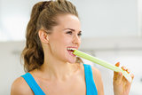 Happy young woman biting celery in kitchen