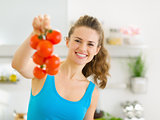 Happy young woman holding bunch of tomato in kitchen