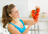 Happy young woman holding bunch of tomato in kitchen