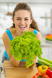 Happy young woman holding green salad in kitchen