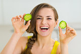 Smiling young woman showing slices of cucumber