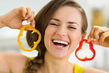 Happy young woman using slice of bell pepper as earrings