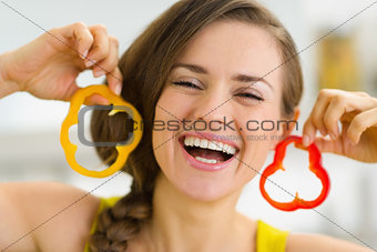 Happy young woman using slice of bell pepper as earrings