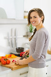 Smiling young housewife cutting vegetables on salad in kitchen