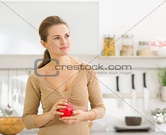 Portrait of thoughtful young woman with apple in modern kitchen