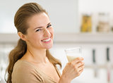 Portrait of smiling young woman with glass of milk in kitchen