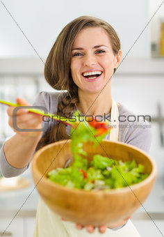 Happy young housewife giving spoon with vegetable salad