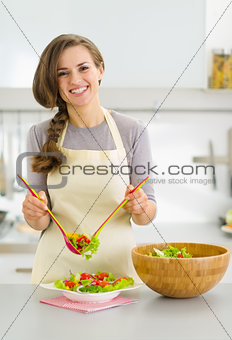 Happy young housewife served plate with fresh vegetable salad in