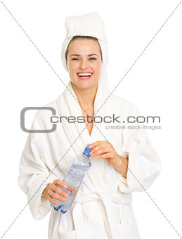 Smiling young woman in bathrobe holding bottle with water
