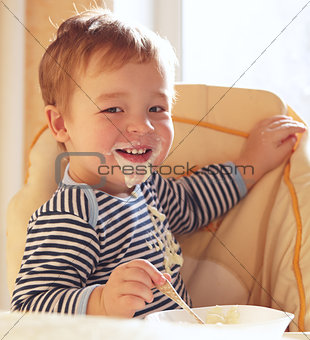 Two year old boy smiles and eating porridge.