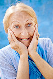 Portrait of surprised senior woman with hands on face on blue ba