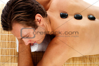Man relaxing on massage bed with hot stones