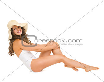 Young woman in swimsuit and hat sitting on floor