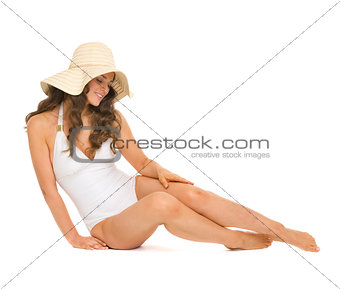 Young woman in swimsuit and hat sitting on floor