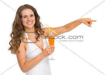 Smiling young woman in swimsuit with cocktail pointing on copy s