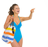 Happy young woman in swimsuit pointing on copy space