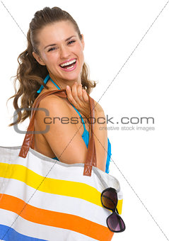 Portrait of smiling young woman in swimsuit with beach bag
