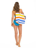 Young woman in swimsuit with beach bag going straight . rear vie