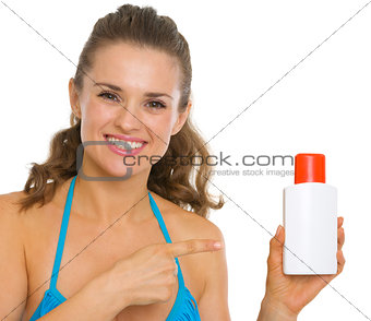 Happy young woman in swimsuit pointing on sun screen creme