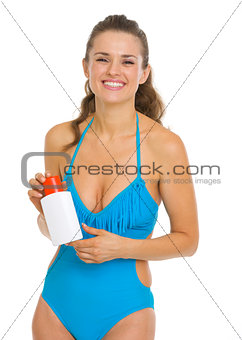 Smiling young woman in swimsuit holding sun screen creme