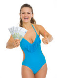 Smiling young woman in swimsuit showing fan of euros