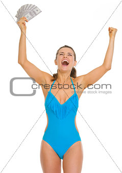 Happy young woman in swimsuit with fan of dollars rejoicing succ