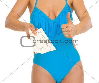 Closeup on young woman in swimsuit showing air tickets and thumb