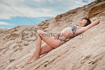 Young thin girl in a swimsuit posing on the sand in the sky.