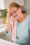 Senior Adult Woman At Kitchen Sink With Head Ache