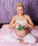 young pregnant woman sitting on bed at home