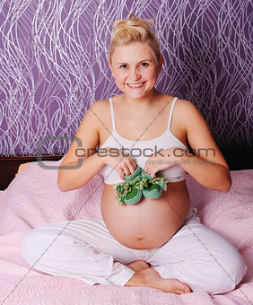 young pregnant woman sitting on bed at home