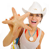 Happy young beach woman in hat showing starfish