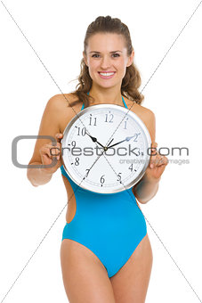 Happy young woman in swimsuit showing clock