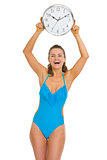 Smiling young woman in swimsuit showing clock