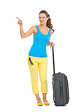 Smiling young tourist woman with wheel bag pointing on copy spac